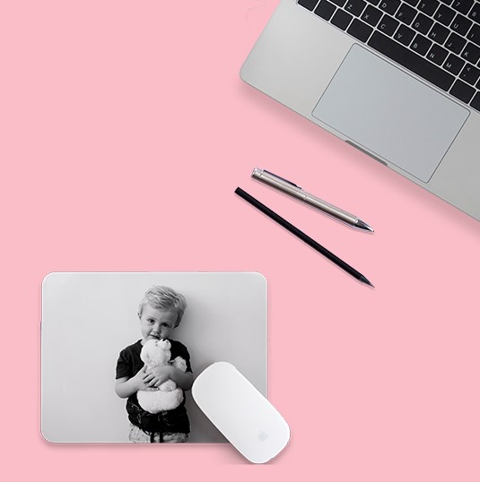 Mouse pad com foto de garotinho segurando um urso de pelúcia. 